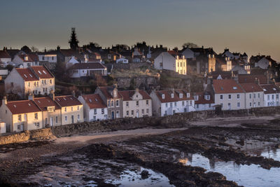 Houses by river in town against sky at dusk