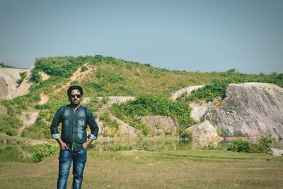 Portrait of young man standing against grassy rock formations