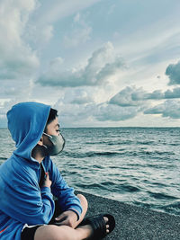 Portrait of young woman sitting on sea against sky