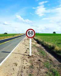 Road sign on field against sky