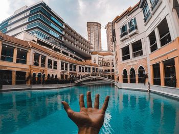 Cropped image of hand reaching towards swimming pool against buildings
