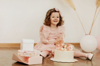 A cute little girl is sitting on the floor with a cake and gifts on her birthday 