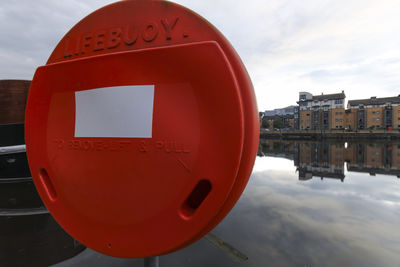 Close-up of information sign on river in city against sky