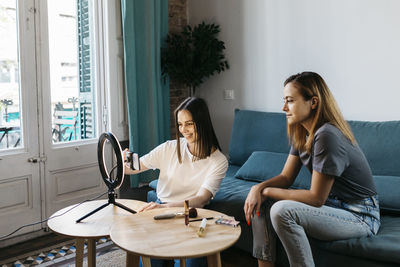 Female influencer vlogging by girlfriend sitting on sofa at home