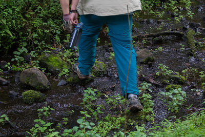 Low section of man holding water bottle while walking on field