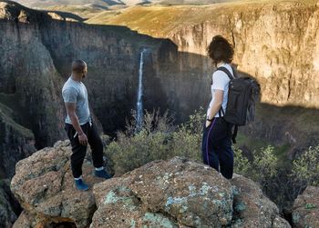 Friends standing on rock while looking at waterfall