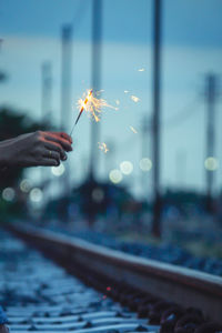 Cropped hand holding sparkler by railroad track