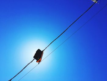 Low angle view of birds perching on cable against clear blue sky