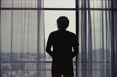 Rear view of silhouette man looking through window