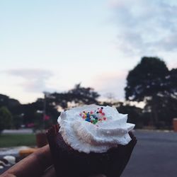 Close-up of hand holding ice cream against sky