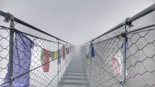 Footbridge over chainlink fence against sky