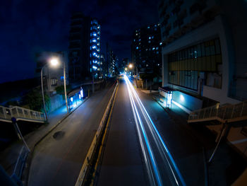 Illuminated light trails on street amidst buildings in city at night