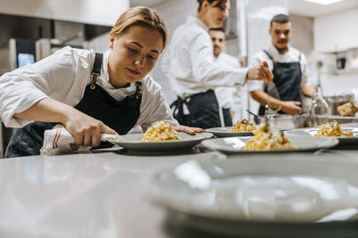 Blond female chef cleaning pasta plate at kitchen counter in restaurant