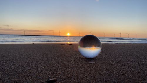 Close-up of crystal ball on beach against sky during sunset