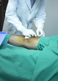 Midsection of doctor injecting in patient knee at hospital