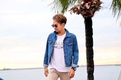 Young man standing by tree against sky