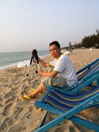 Portrait of man sitting on beach against clear sky