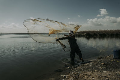 Man fishing in lake against sky