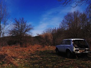 Abandoned car on field against blue sky