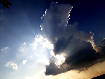 Low angle view of sunlight streaming through clouds