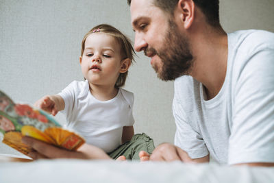 Happy father and baby girl little daughter having fun reading a book in children room at home