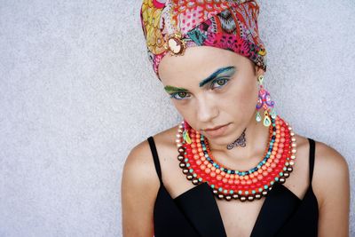 Portrait of confident young woman wearing headscarf and jewelries against wall