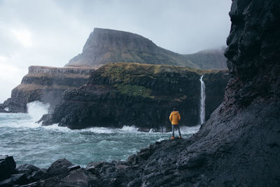 Man standing on cliff by sea against sky