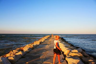 Woman standing on jetty against clear sky at beach