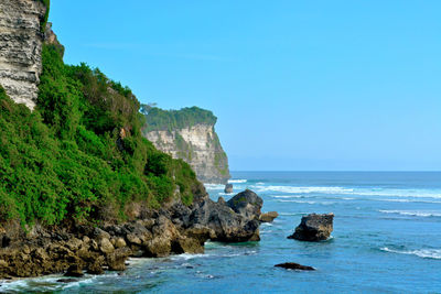 Scenic view of rocks by sea against blue sky