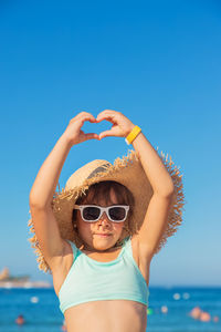 Portrait of young woman wearing sunglasses while standing at beach against clear blue sky