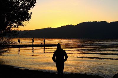 Silhouette woman standing by lake against sky during sunset