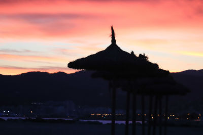 Silhouette built structure by sea against orange sky
