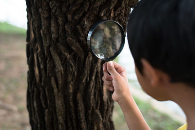 Close-up boy looking at tree through magnifying glass
