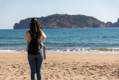 Rear view of woman standing at beach against sky