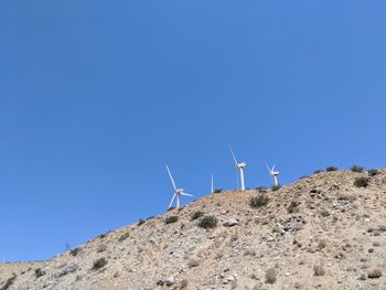 Low angle view of windmill on landscape against clear blue sky