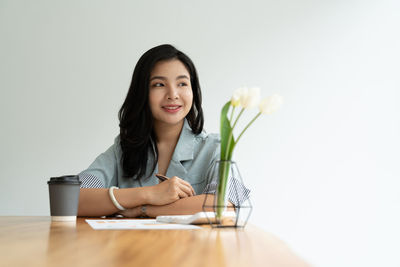 Portrait of young woman using mobile phone while sitting against white background