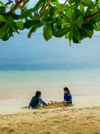 People sitting on beach by sea against sky