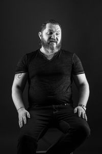 Portrait of young man sitting against black background