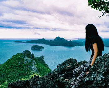 Woman standing on rock by sea against sky