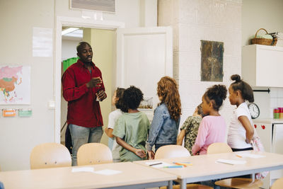 Male teacher guiding and explaining students at doorway in classroom