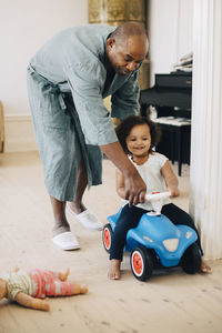 Full length of father playing with daughter on toy car in living room at home