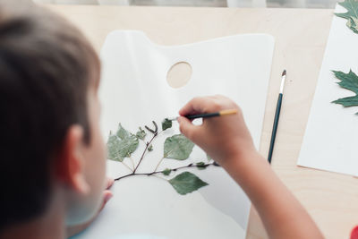 Close up of child sitting at desk and making picture from dry birch leaves. autumn activities 