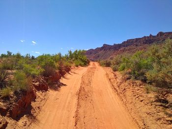 Dirt road amidst land against clear blue sky