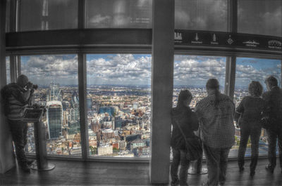 People in city against sky seen through window