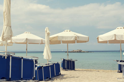 Lounge chairs and parasols on beach against sky