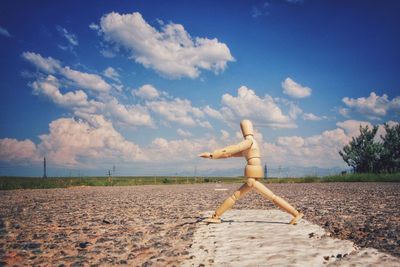 Wooden figurine on road against sky