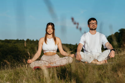 Young adult couple meditating outdoors, caucasian woman and man dressed alike breathing fresh air