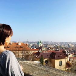 Rear view of man looking at city buildings against clear sky