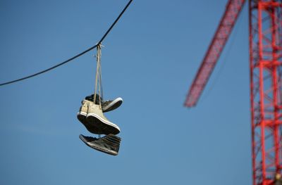 Pairs of shoes hanging on cable against clear blue sky