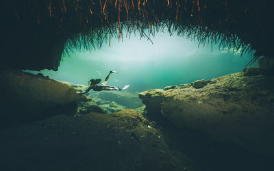 Woman swimming underwater by rock formation 